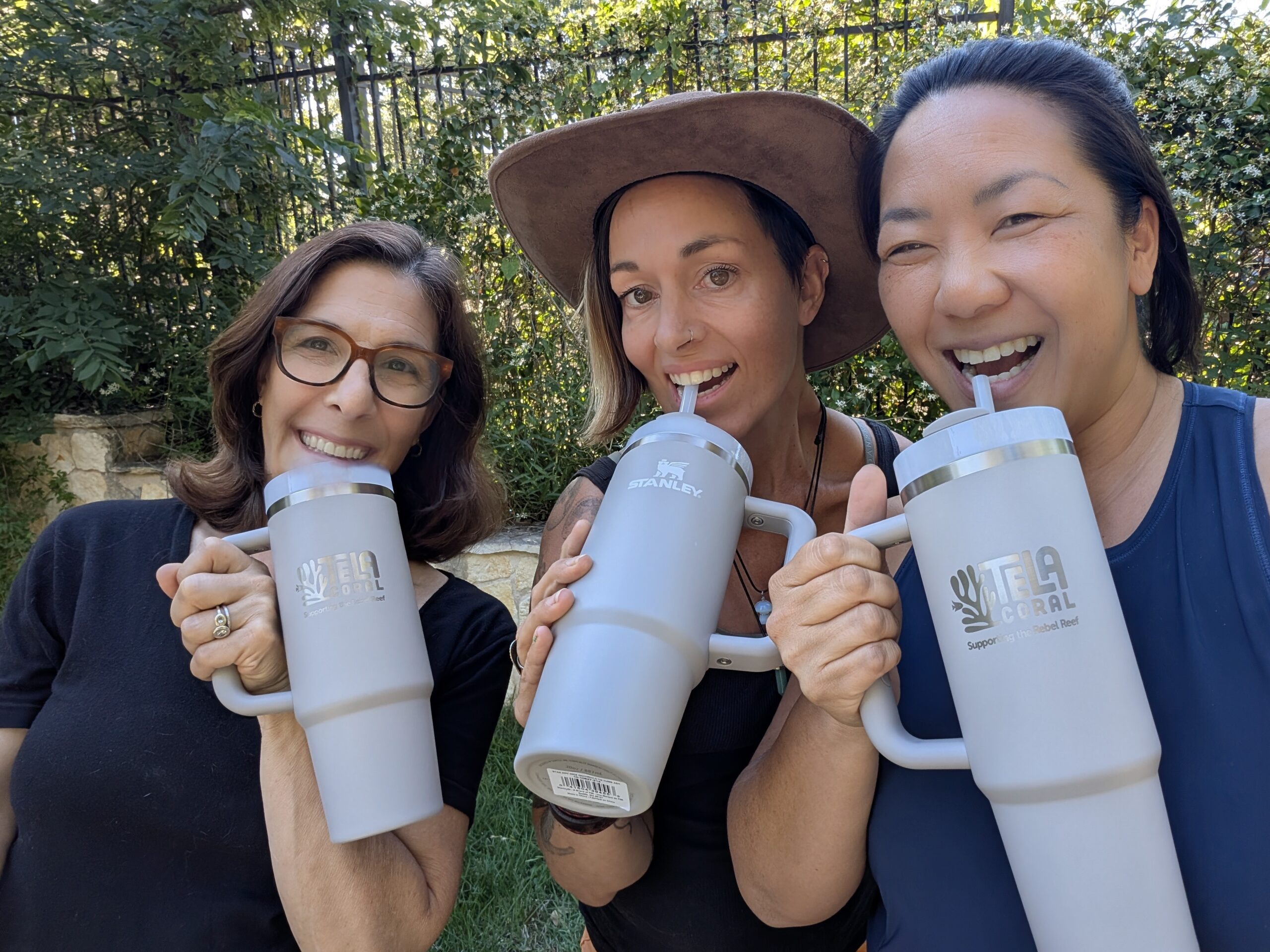Three women smile holding special edition Stanley tumblers emblazoned with the "Tela Coral" logo.
